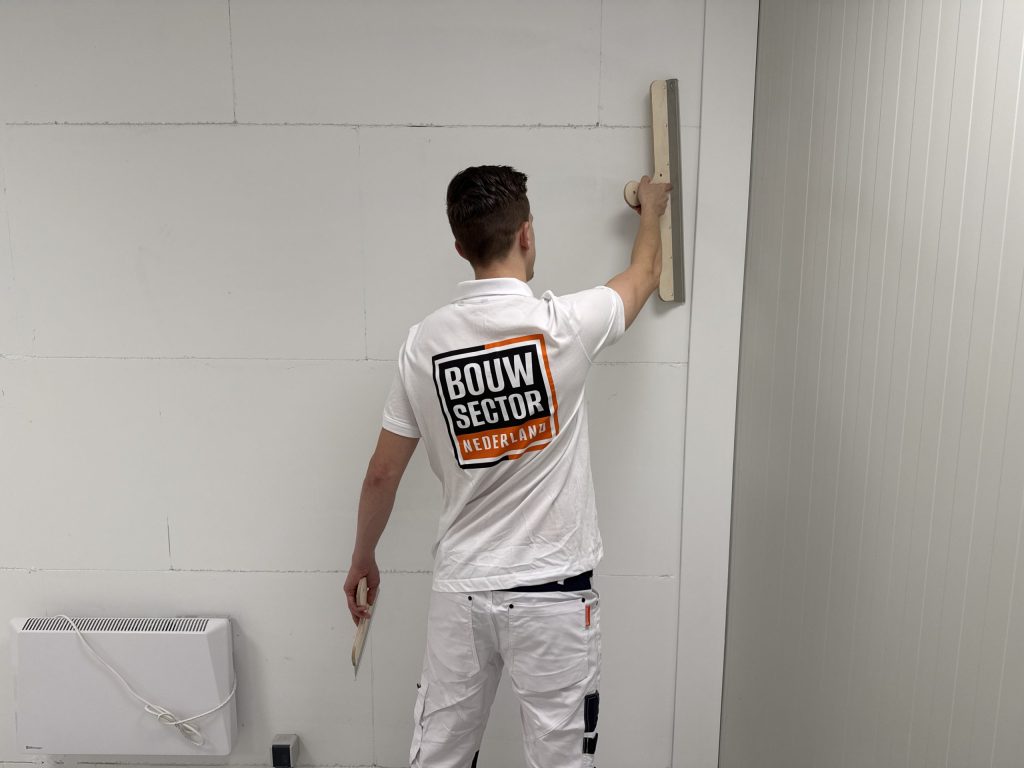 Stukadoor van Bouwsector Nederland zet een lange spaan tegen een gipsplaatwand met zichtbare plaatnaden